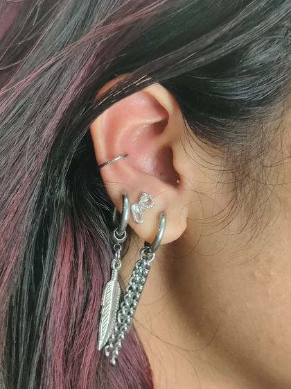 A close-up of a healed ear curation with a helix piercing and multiple lobe piercings featuring chain and feather dangles. We have a wide variety of jewelry for healed piercings.