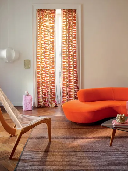 An alternate view of the art-inspired living room, featuring the striking orange sofa alongside a modern sling chair. This composition highlights how our custom upholstery can anchor a space filled with eclectic and expressive design elements.