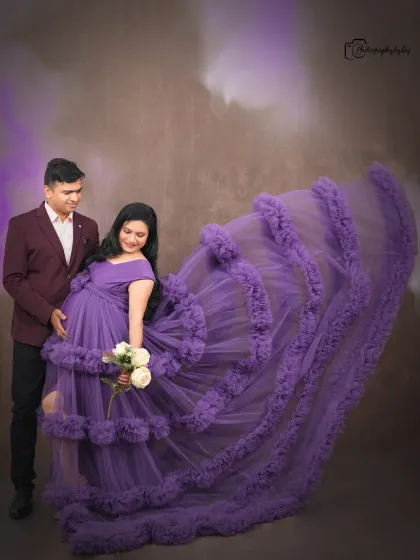 A glamorous studio portrait of a couple, with the mother-to-be in a purple ruffled gown. The flying fabric adds a dramatic touch.