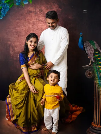 The family of three, soon to be four, poses for a regal portrait. The older son's bright yellow kurta adds a pop of joyful color to the classic, elegant scene.