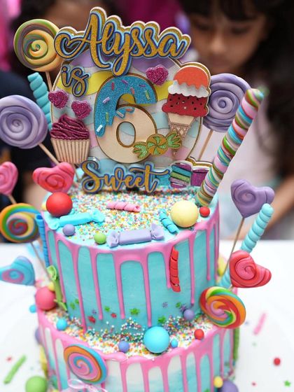 A close-up of the "Sweet 6" candy-themed cake for Alyssa. This two-tier drip cake is covered in lollipops, candies, and an ice cream cone.