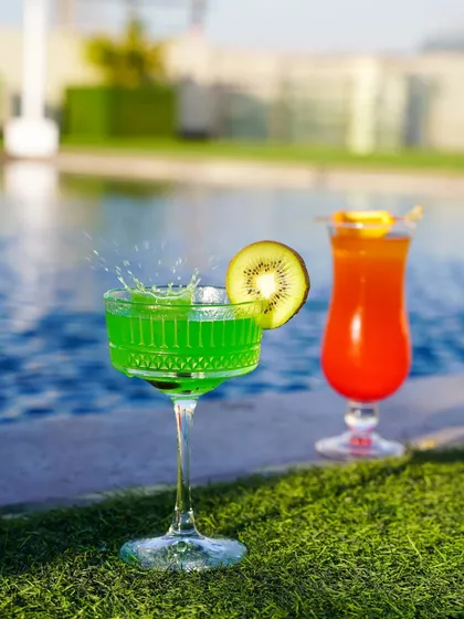 A vibrant green kiwi cocktail with a splash captured mid-action, set by a swimming pool. This shot combines dynamic action with a relaxing summer setting, ideal for hotel and resort promotions.