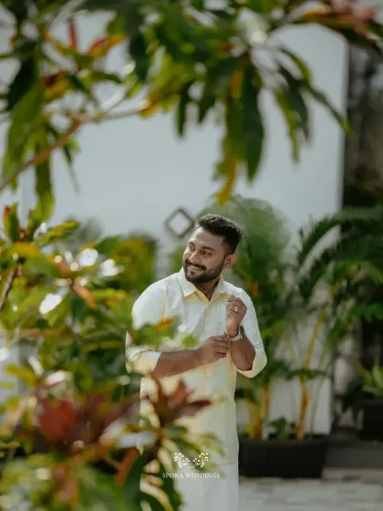 A portrait of the groom looking happy and relaxed, framed by the lush greenery of a traditional Kerala venue.