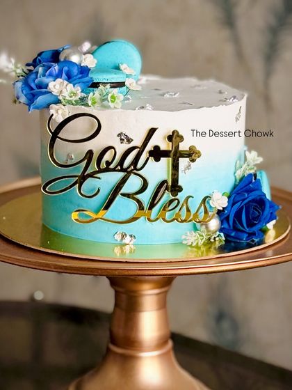 A "God Bless" tall cake in a blue ombre design for a religious ceremony. This chocolate truffle cake is decorated with blue roses and macarons.