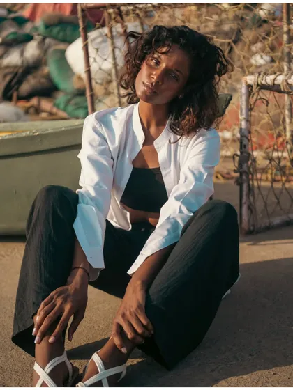 A relaxed, seated portrait in a rustic, industrial beach setting. The warm sunlight gives the shot a natural and approachable feel.