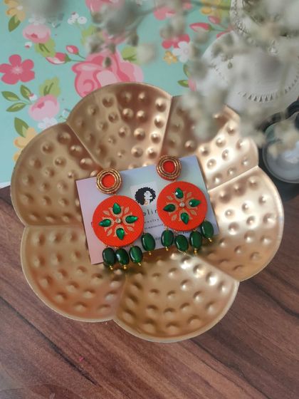 These hand-painted earrings feature a vibrant orange base with green zardozi embroidery and bead drops. They are perfect for adding a pop of color to your look.