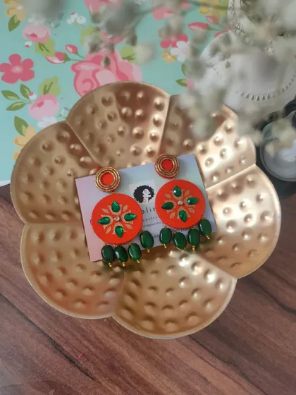 These hand-painted earrings feature a vibrant orange base with green zardozi embroidery and bead drops. They are perfect for adding a pop of color to your look.