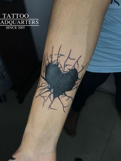 A striking tattoo of a solid black heart with cracks spreading outwards, creating a powerful visual effect.