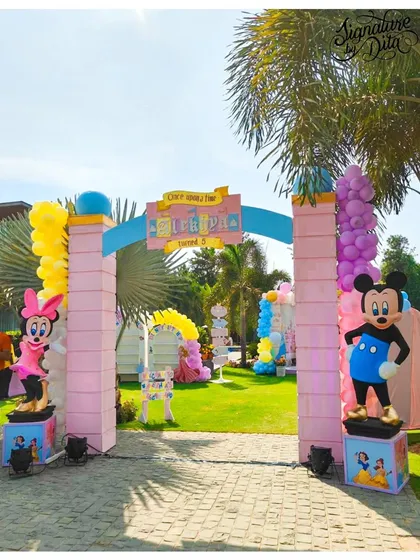 The grand entrance to the Disneyland party, flanked by statues of Mickey and Minnie Mouse. The pastel pink archway welcomes guests to a magical celebration.