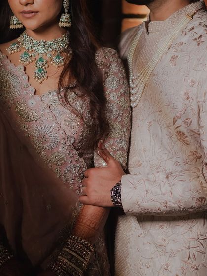 A close-up shot focusing on the couple's hands and torsos, highlighting the beautiful details of their pastel pink and ivory outfits. It’s a subtle yet intimate portrait.
