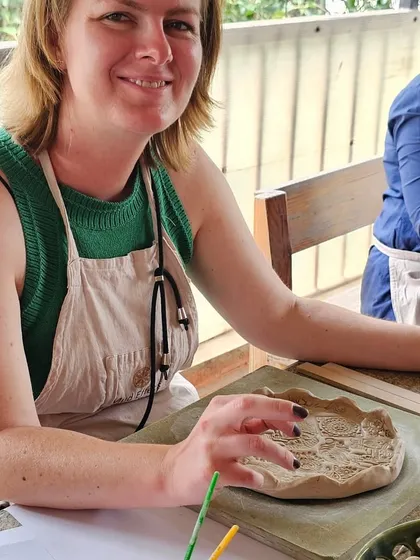 A participant from a corporate workshop smiling as she works on her hand-built plate. These sessions are always filled with happiness and laughter.