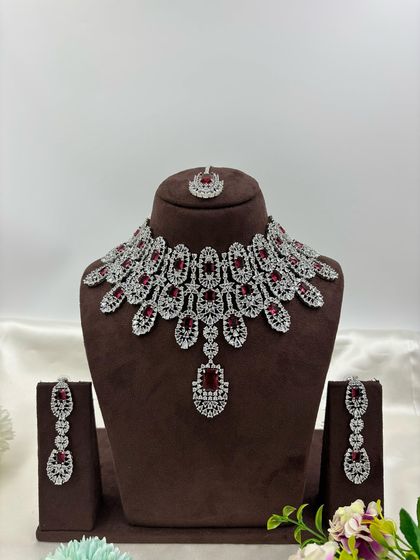 A full-coverage AD bridal set with a matching maang tikka. This silver-plated design is available in a wide range of colors like green, blue, pink, and white, making it a versatile choice for weddings.