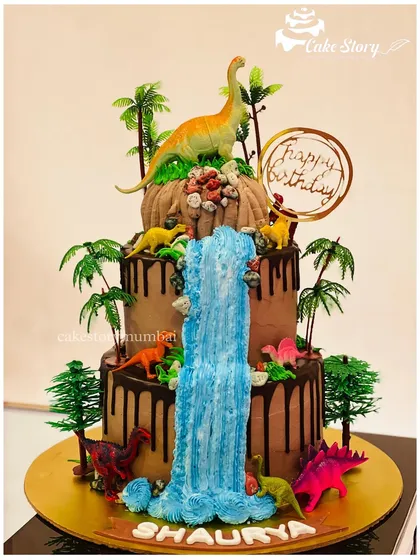 A spectacular three-tier dinosaur cake with a cascading waterfall. This detailed design features various dinosaurs in a prehistoric jungle setting, creating a stunning centerpiece.