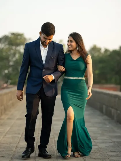 A happy couple walking arm-in-arm across a stone bridge, captured during a golden hour pre-wedding shoot.