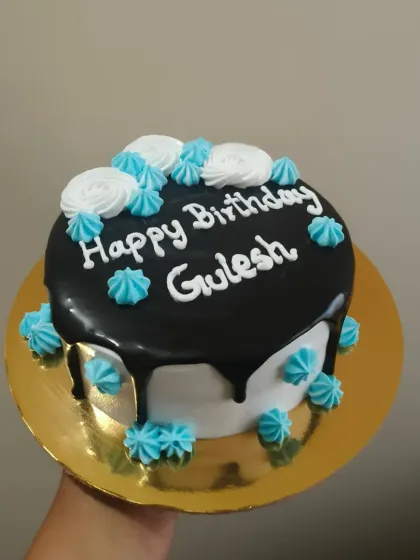 A mini drip cake with a dark chocolate ganache and contrasting blue and white piped details.