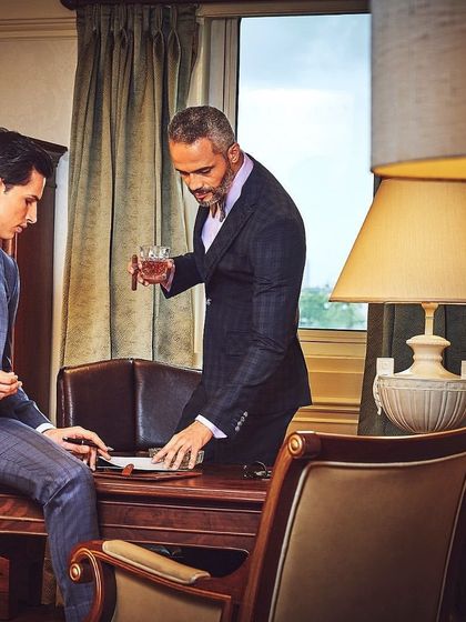 This scene from a SPAADAA campaign was styled to tell a story of mentorship and legacy. The sharp, tailored suits on both models establish a clear dynamic of power and respect in a classic, luxurious environment.