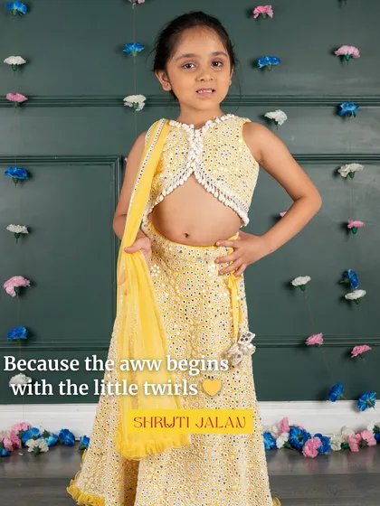 Because the "aww" begins with the little twirls. A girl is captured mid-twirl in a sunny yellow mirror-work lehenga, full of joy and movement.