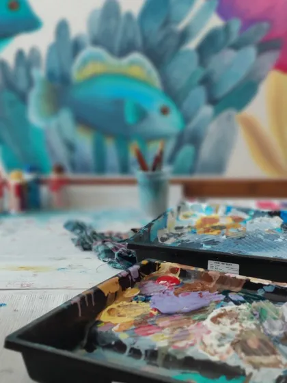 The beautiful mess of creation. Paint palettes filled with color, with a mural taking shape in the background.