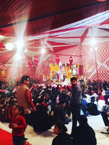 Another angle of a large Guruji satsang, showing the crowd of devotees and the expansive tent decoration with red and white fabrics and paper lanterns.
