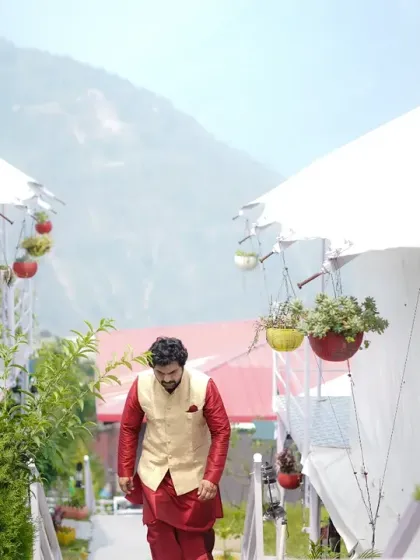 The groom's entrance. This shot captures him walking down a path lined with modern tents at a destination wedding, creating a sense of anticipation.