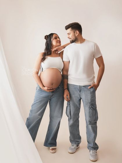 A cool and casual couple portrait. Dressed in jeans and white tops, their relaxed pose and loving gaze make for a stylish and modern maternity photo.