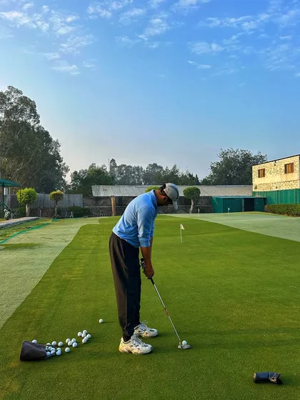 A golfer lines up a putt on the green, with a full bag of practice balls beside him.