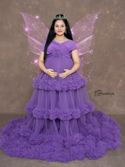A magical studio portrait with edited-in fairy wings. The mother-to-be looks ethereal in a purple ruffled gown.