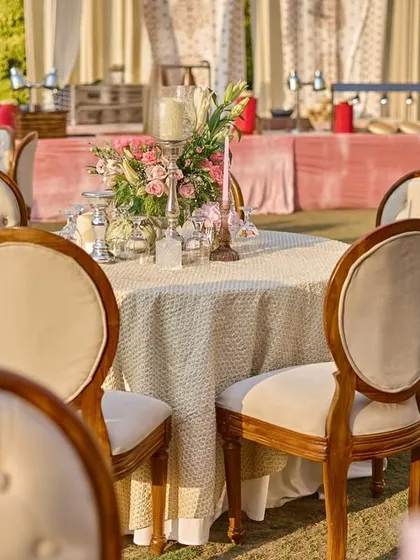 An elegant outdoor dining setup with classic wooden chairs and tables dressed in fine linen, with a simple yet beautiful floral centerpiece.