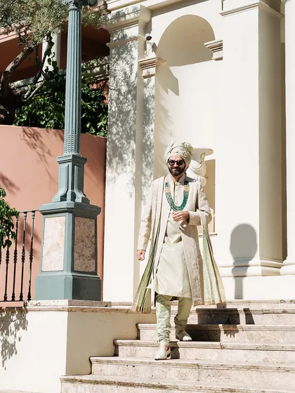 A confident stride down the steps in Marbella. The groom's open-jacket Tarun Tahiliani sherwani was chosen to be both stylish and comfortable for a warm destination wedding.