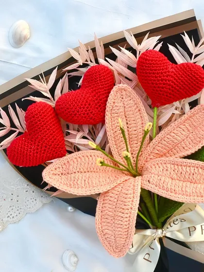 A unique romantic bouquet featuring a soft pink crochet lily surrounded by three bold red hearts. It's a beautiful blend of elegance and love.