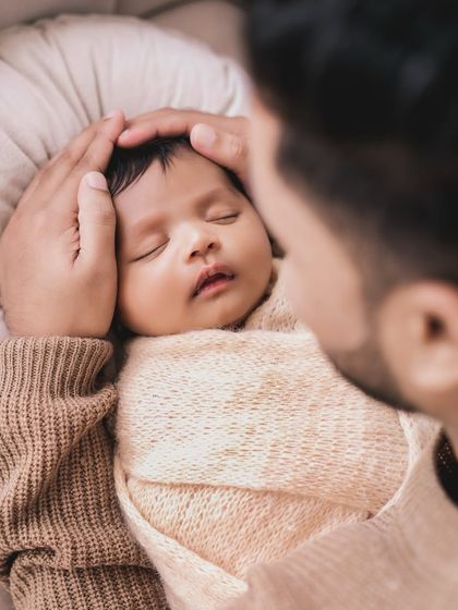 A close-up over-the-shoulder shot of a father looking at his swaddled newborn.
