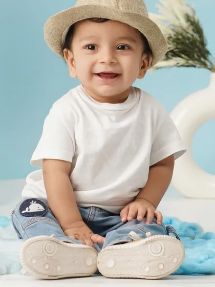 A sweet close-up of a smiling baby boy in a summer hat, captured during his blue-themed first birthday session.