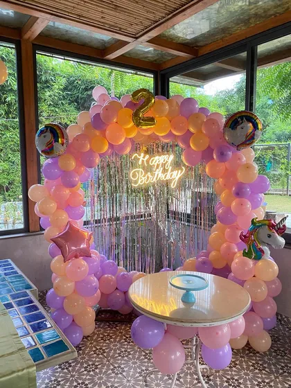 A unicorn-themed second birthday party with a circular balloon arch in pastel orange and purple.