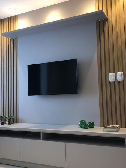 A minimalist TV unit design featuring vertical wooden slats and a floating console. The overhead shelf with spotlights provides perfect accent lighting, making the entertainment wall a stylish focal point.