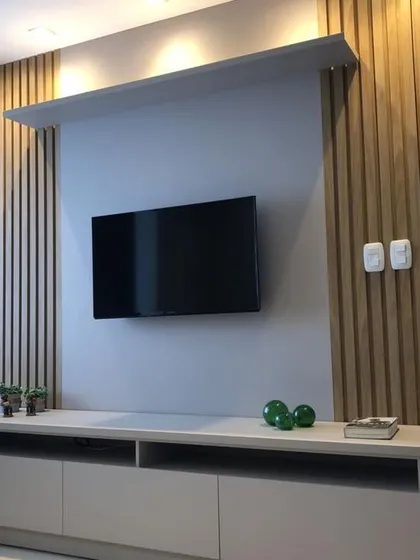 A sleek and modern TV unit design. This unit combines a simple grey console with natural wood-fluted paneling and an overhead shelf with spotlights, creating a stylish focal point for the living room.