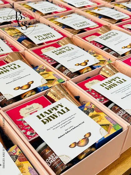 An overhead view of Diwali gift boxes being prepared for a corporate client. Each box contains a curated selection of treats and a personalized festive card, demonstrating the care put into every single hamper.