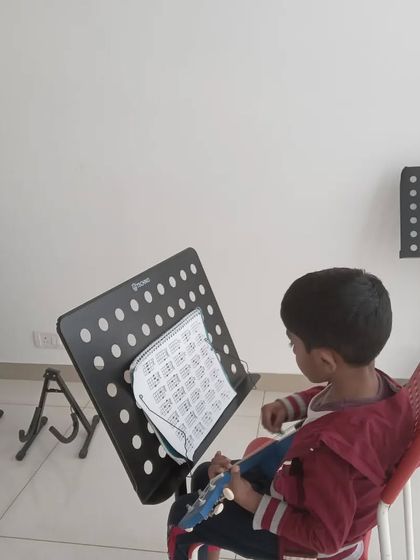 A young student with his ukulele, focused on his sheet music. We provide all the necessary equipment for a great learning experience.