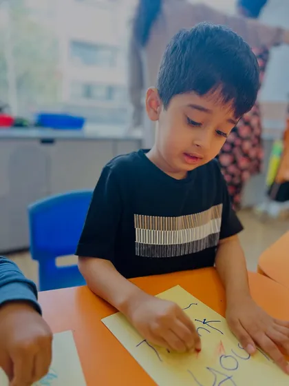 Another student carefully writes "Thank You" on his card. This activity reinforces positive social sentiments while also practicing fine motor control and writing.