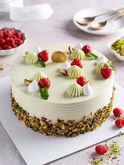 Our Pistachio Raspberry Cake, a full view of its simple elegance. The pale green frosting is garnished with fresh raspberries and mini meringues, with a base of crushed pistachios for texture and flavour.