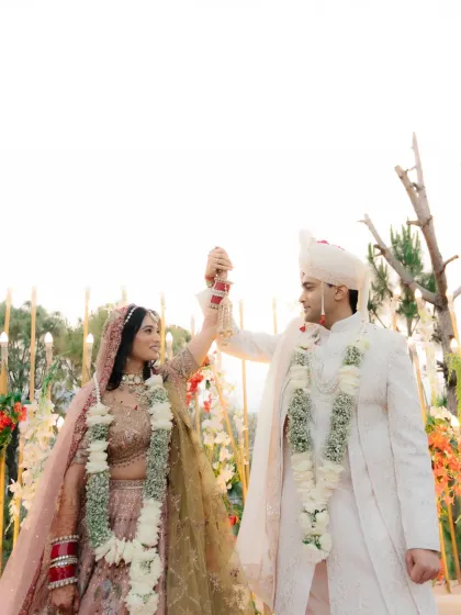 A playful moment during the varmala ceremony, where the couple joyfully raises their hands.
