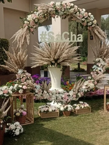 A rustic-chic circular wedding arch, perfect for photo opportunities. This piece is crafted with a mix of pampas grass and delicate pastel roses, and can be personalized with custom lettering like the '#SaCha' hashtag shown here.