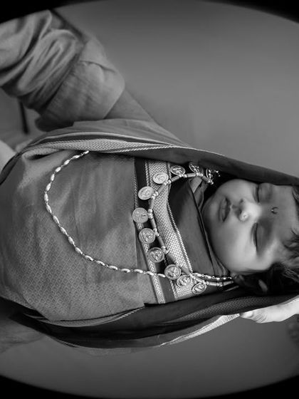 A creative black and white shot of a newborn in a traditional Maharashtrian outfit, held by her parents to create a feeling of being cradled in a womb.