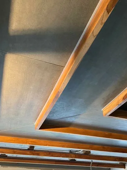 A detail of the ceiling structure in the Lucknow penthouse, where wooden beams intersect with the darker ceiling panels, creating a geometric pattern that echoes the room's partitions.