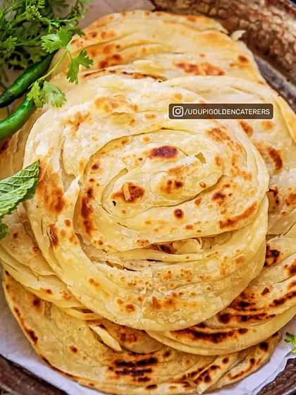 A beautiful stack of flaky, layered Kerala Parottas. Each parotta is skillfully hand-rolled and cooked on a hot tawa until golden, creating a soft yet crispy texture that pairs wonderfully with our vegetarian curries.