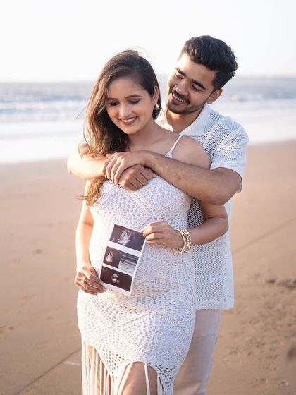 A sweet pregnancy announcement on the beach. The couple holds their sonogram picture while sharing a loving embrace, with the gentle waves behind them.