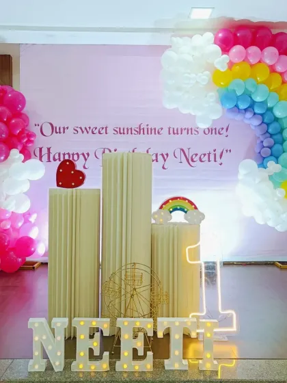 A full view of the rainbow and sunshine themed first birthday. The setup includes a large backdrop, a colorful balloon rainbow, and tall plinths for the cake, all designed to create a joyful atmosphere.