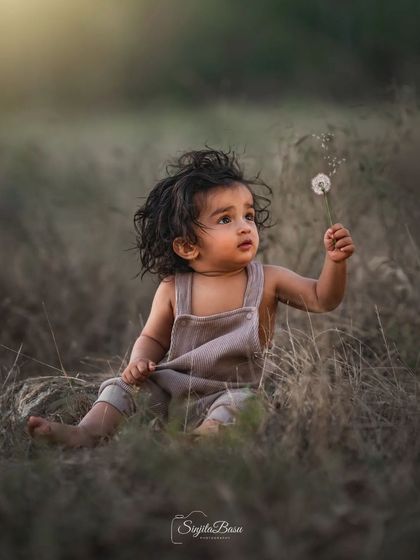 A baby sitting in a field, mesmerized by a dandelion. This image captures the quiet curiosity and gentle spirit of a child discovering the small wonders of the natural world.