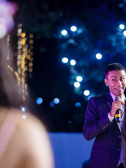 A guest delivers an animated and joyful speech, with beautiful bokeh lights in the background. These are the moments of laughter and storytelling that make a wedding unique.