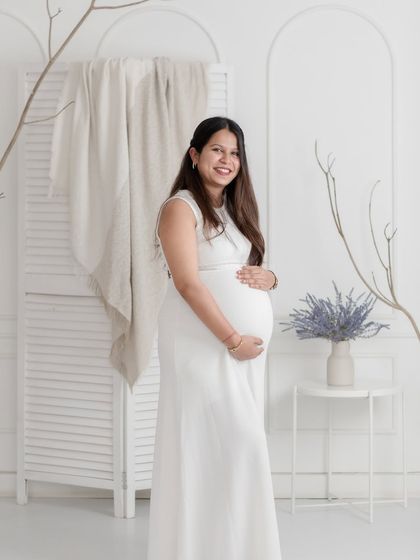 A radiant solo portrait of an expectant mother in a simple white dress, her happiness shining through.