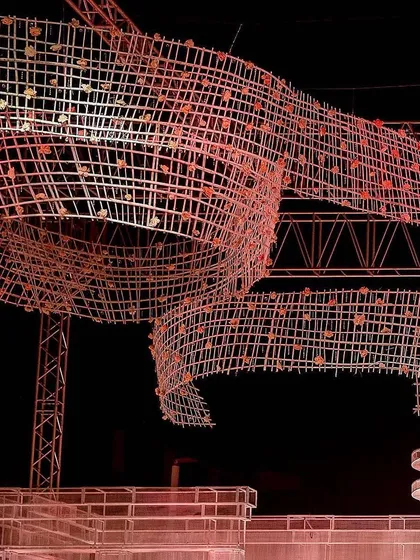 The intricate, ribbon-like ceiling installation seen from below, glowing with a warm pink light. This view showcases the complexity and scale of the custom-built structure.